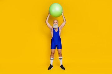 Full length photo of joyful strong masculine trainer raise ball intense cardio regime spend time gym isolated on yellow color background