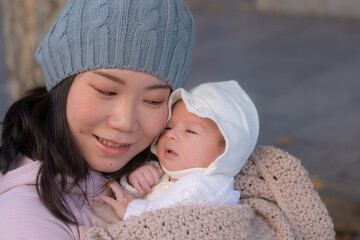 outdoors urban lifestyle portrait of young happy and beautiful Asian Chinese woman as mother of little adorable baby girl holding her tender and sweet in city street on sunny Winter day