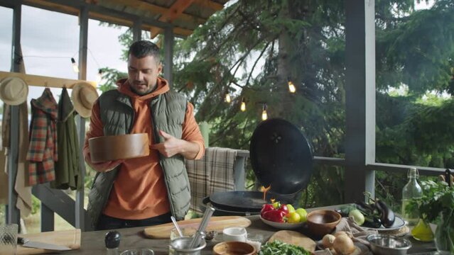 Food blogger telling recipe on camera and showing bowl with red cabbage cole slaw salad while giving culinary masterclass on outdoor barbecue terrace