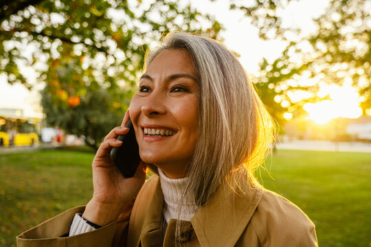 Mature asian woman talking on mobile phone while strolling in park