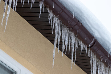 Big icicles on the roof of a townhouse.  Roof of home covered with icicles in winter. Dangerous problem