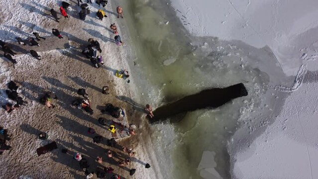 the drone flies over the hole in the winter rake, the river is covered with ice, people enter the cold water, cross themselves and plunge headlong into the ice water three times
