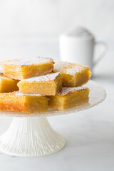 Lemon squares piled high on a pedestal stand with powdered sugar in behind.