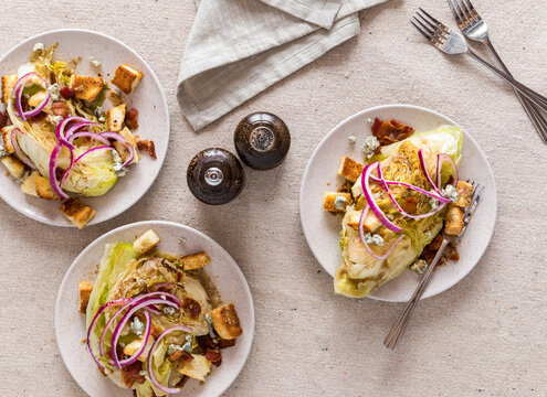 Plates Of Crisp Warm Wedge Salad Topped With Bacon, Croutons And Red Onion.