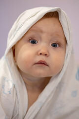 Pretty baby girl wearing towel on head sits and waits for parent. Baby daughter with amused expression wants to dry at home
