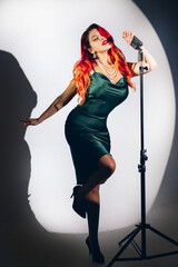 Glamour red haired lady singing with microphone on the dark stage background