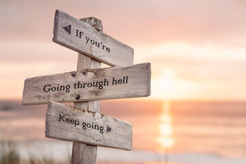 if youre going through hell keep going text quote engraved on wooden signpost outdoors at the beach. Sunset theme.