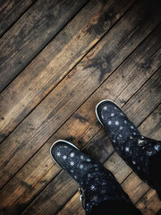 Close up of a pair of winter shoes on a rustic wooden background with copy space. Person walking on the wooden bridge. Top view on the legs in warm black boots.