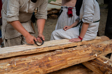 Man carpenter using drawknife - vintage analogue of spokeshave and plane to shape and smooth wood board at summer historical medival festival - close up. Craftsmanship, handwork concept