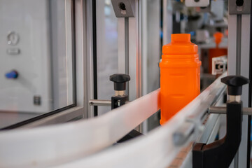 Empty orange plastic jerrycan moving on conveyor belt of automatic pet blow molding machine at factory, exhibition - close up. Manufacturing, recycling, industry, technology equipment concept