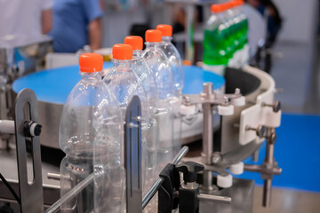 Row of empty pet lemonade bottles with orange caps on conveyor belt of automatic liquid filling machine at plastic exhibition - close up. Manufacturing, industry and technology equipment concept