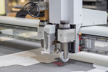 Digital flatbed cutter, plotter cutting white cardboard sheet at printer exhibition, trade show - close up. Technology, industrial, manufacturing, robotic, electronic concept
