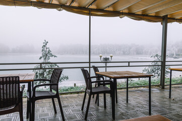Empty tables outdoors in a cafe by the lake in winter. View of the lake in winter from the cafe. Ice on the lake in winter. Landscape with a view of the frozen lake from the cafe.