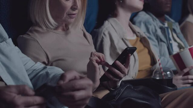 Mature Caucasian man and woman switching their smartphones off in cinema