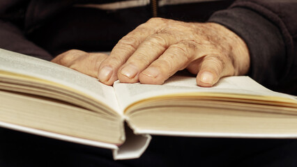 An elderly man, a grandfather, holds an open book in his hands. Leisure for the elderly. Reading a book