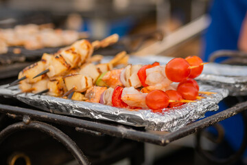 Cooked scallop and shrimp, prawn skewers, cherry tomato on foil at summer local food market - close up. Outdoor cooking, gastronomy, seafood, street food concept