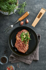 Steaks. Sliced grilled meat steak New York or Ribeye with spices rosemary and pepper in iron pan black on marble board on old wooden background. Top view. Mock up.