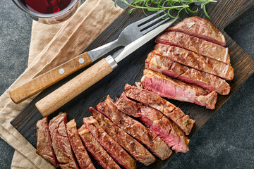 Steaks. Sliced grilled meat steak New York or Ribeye with spices rosemary and pepper on black marble board on old wooden background. Top view. Mock up.