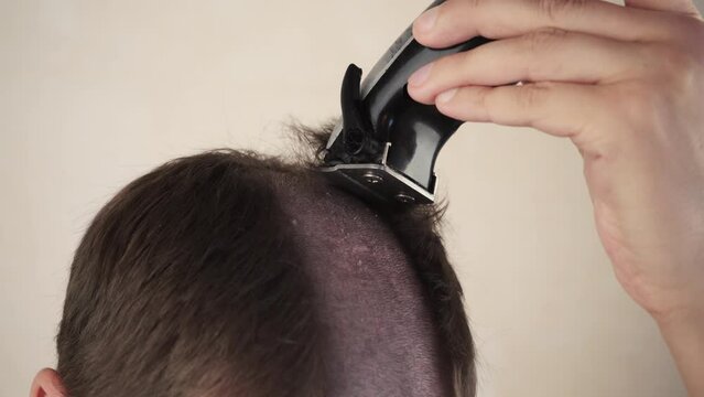 A handsome man cuts his own hair with a trimmer, a machine at home. Self-service during quarantine isolation. Stay home, hairdresser. haircut before chemotherapy.