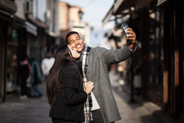 Multiracial couple posing on narrow streets in old part of the sity. Taking selfy photo with phone....
