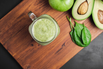 Green smoothie drink blended in a glass jar, avocado, spinach leaves and apples at wooden board,...