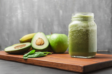 Green smoothie drink blended in a glass jar, avocado, spinach leaves, banana and apples at wooden...