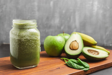 Green smoothie drink blended in a glass jar, avocado, spinach leaves, banana and apples at wooden board