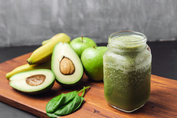 Green smoothie drink blended in a glass jar, avocado, spinach leaves, banana and apples at wooden board