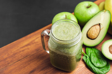 Green smoothie drink blended in a glass jar, avocado, spinach leaves, banana and apples at wooden...