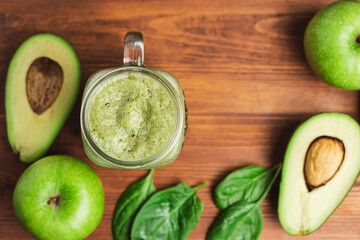 Green smoothie drink blended in a glass jar, avocado, spinach leaves and apples at wooden board, top view