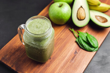 Green smoothie drink blended in a glass jar, avocado, spinach leaves, banana and apples at wooden...