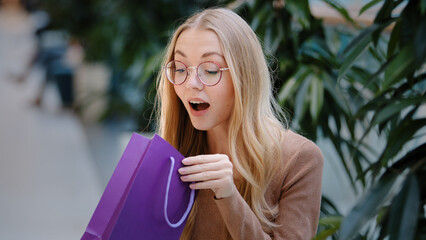 Portrait excited shocked amazed surprised Caucasian woman with glasses looking inside gift bag...