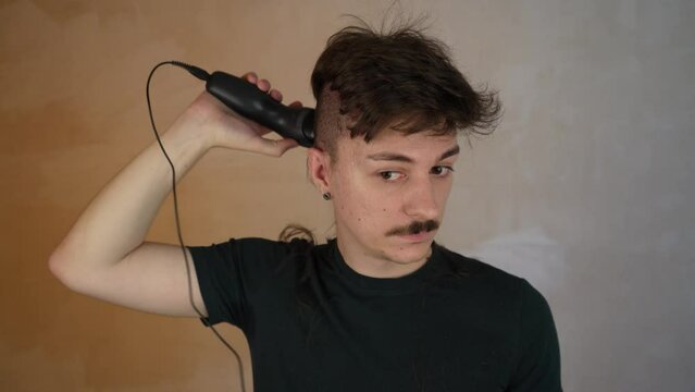 A man in the process of cutting his own hair. Cuts hair very short while the hair on top is still quite long. Electric hair clippers cutting the back and side of the head during the corona virus