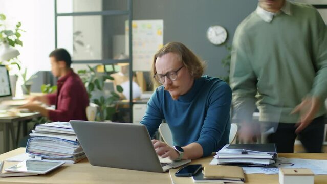 Timelapse of overloaded businessman using laptop while colleagues stacking papers on his desk during workday in office
