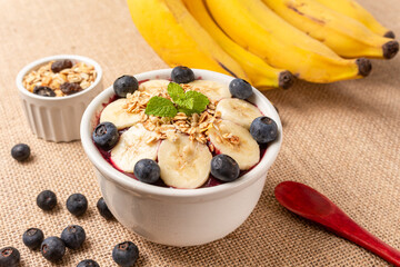 Acai bowl with banana, blueberry and cereal on burlap cloth.