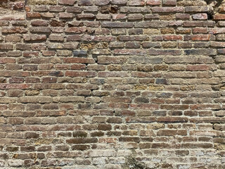 Old worn brick wall, rough textured, shattered and distressed surface. Ancient primitive abandoned weathered wall.
