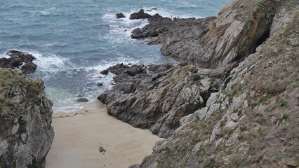 Fototapeta na wymiar Falaises près d'une mer agité, sous un ciel nuagueux, gris et menaçant, eau fracassant contre les rochers, falaises en roches et de la verdure et végétation, côté bretonne, coin de la Bretagne
