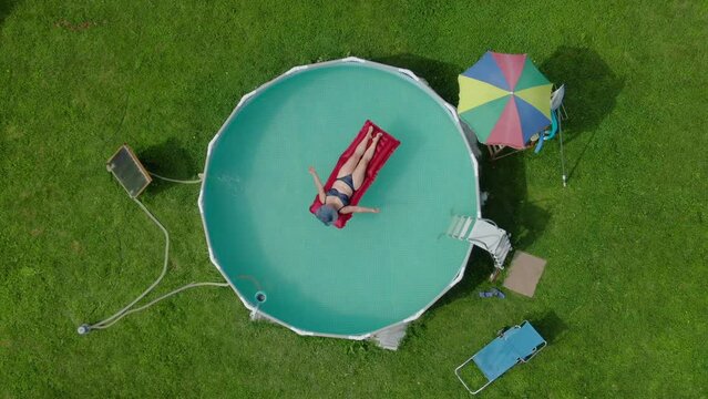 Aerial view of a woman in a hat swimming in round pool on the inflatable matrass
