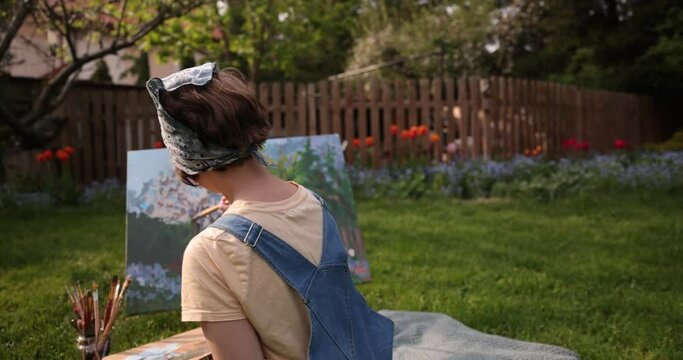 Creative girl is painting a beautiful picture in the garden, holding a palette and brush, using tools to create a canvas . Artists and artwork concept