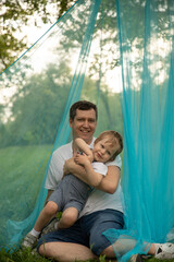 Father and son in nature play in a fabric tent, a boy and a man at a picnic celebrate a birthday, hug, rejoice on Father's Day