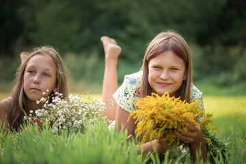 Two beautiful young girls lie on the grass in a summer field.