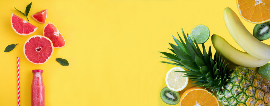 Grapefruit smoothie in a glass bottle and tropical fruits on the yellow background. Banner. Copy space. Top view.