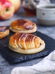 Pieces of traditional French thin apple tartlet on a black plate with it fruits and cup of tea in background. A dessert made with puff pastry pie, caramelized with brown sugar