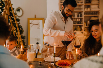 Joyful man pouring wine into glass during family Christmas dinner