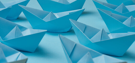 A group of blue paper boats on a blue background. The concept of a controlled crowd