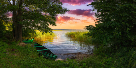 Sunset on the shore of the lake and green boats in the reeds.