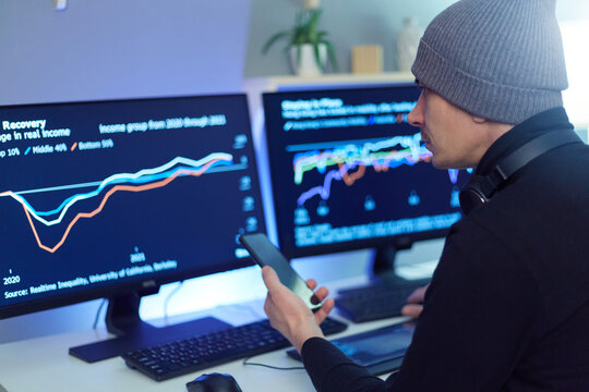 Side view of hipster business man trader analyst looking at laptop monitor, investor broker analyzing indexes, financial chart, trading online, holding smart phone for surching information.
