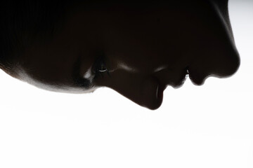 Fashion and make-up concept. Close-up dark face silhouette of beautiful and sexy woman. Part of model face illuminated with light. Sensual mood. Eye is in camera focus