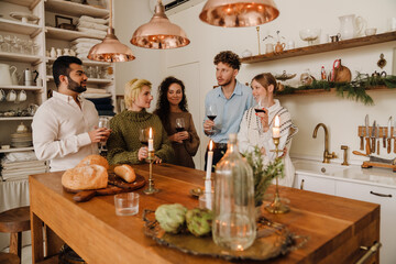Group of smiling friends drinking wine and talking while celebrating Christmas together