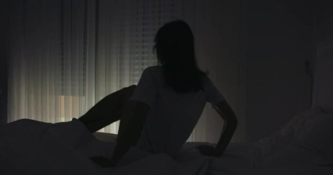 Young woman wake up in the morning and sitting on bed while automatic roller shutter open the window